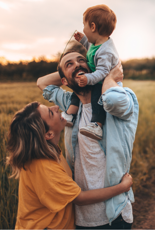 couple holding toddler on mans shoulders in field